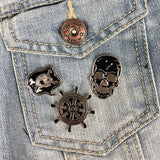Een drie zwart met zilverkleurige pins van een doodskop tekstwolk met schedel en een  klassiek schipsroer op een borstzakje van een blauw spijkerjasje