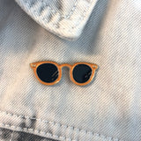 Oranje zonnebril pin op een licht spijkerjasje