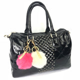 twee pompoms creme en roze aan goudkleurige clips en sleutelhanger ringen met tekstplaatjes met de tekst megamooi aan een zwarte lak handtas