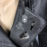 close up van vier zwart met zilverkleurige pins drie hebben afbeeldingen van een doodskop en een is een pin van een gevechtsbijl