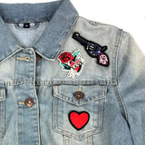 Close-up van een grijze pistool patch een rood hartje met zwarte rand patch en een rode love tattoo patch op een blauwe spijkerstof jas
