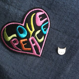 Pin van een witte poezenkop samen met een love peace strijk patch op een blauwe ondergrond.Witte Poes Kat Emaille Pin samen met een love peace patch op een blauwe ondergrond